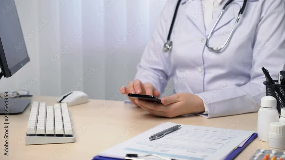 Female doctor typing on smartphone, texting a patient, using medical app. Healthcare and medicine