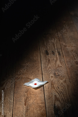 Fototapeta Naklejka Na Ścianę i Meble -  Used bandage with blood fallen on wooden floor in strip of light. Top view.