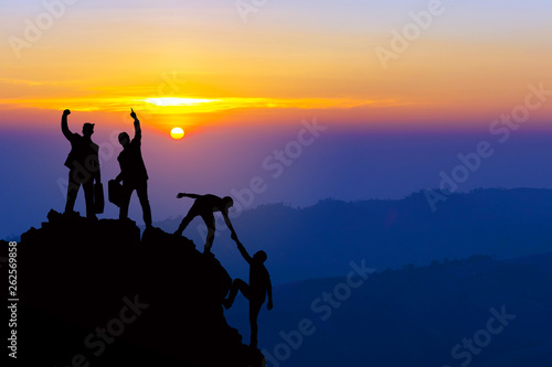 Teamwork friendship hiking help each other trust assistance silhouette in mountains, sunrise. Teamwork of four men hiker helping each other on top of mountain climbing team beautiful sunrise landscape