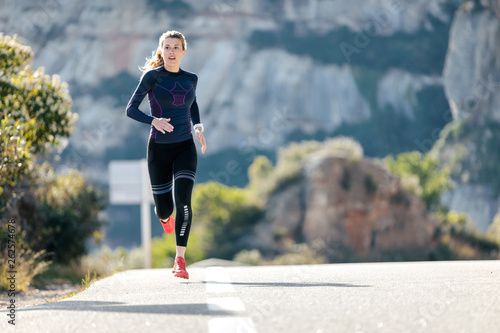 Sporty young woman running on mountain road in beautiful nature. photo