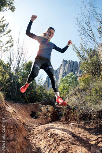 Young fitness woman trail runner running and jumping on rocky mountain.