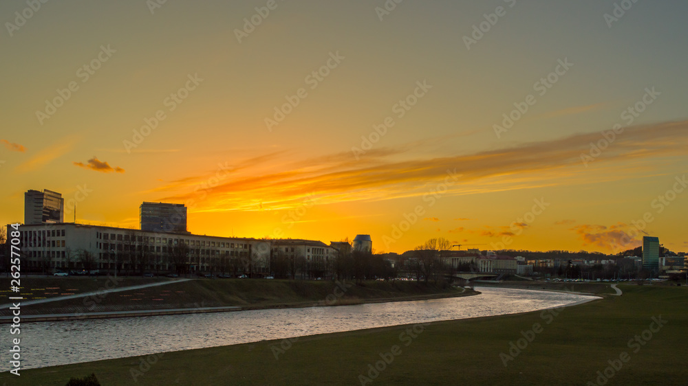 A beautiful orange sunset over a river and buildings silhouettes in Vilnius city center