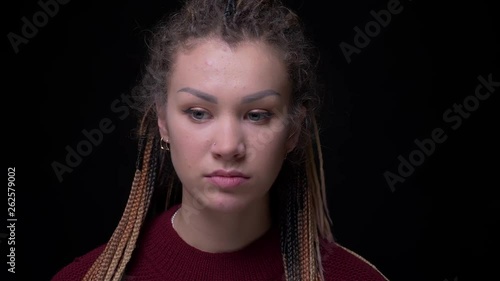 Pretty brunette girl with piercing and dreadlocks watches miserably and sadly into camera on black background. photo