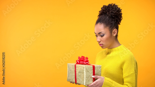 Sad young female looking present in hands, holiday gift disappointment, surprise © motortion
