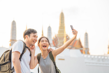 Asian blogger couple travel in Bangkok, Thailand, sweet couple using mobile phone selfie and photo view while spending sweet time in holiday trip in sunset. Couple travel in city concept.