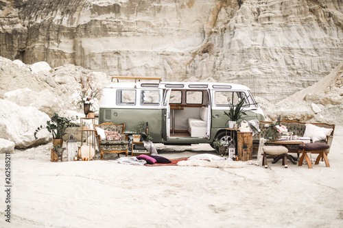 Wedding decor in boho rustic style. Green hippie bus, decorated sofa, armchair, carpets, pillows, table with candles, succulents, plant decoration on the background of canyon landscape