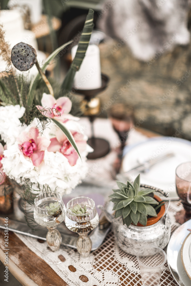 Beautiful glasses, candles, flowers stand on a fruitful decorated table in rustic boho style. Bright composition of flowers with a decor in the style of the rustic
