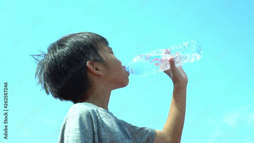 Slow motion young Asian boy drink water from a bottle under blue sky white cloud in summer Slow motion young Asian boy drink water from a bottle under blue sky white cloud in summer