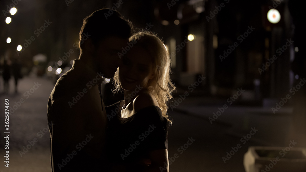 Blond female teasing and cuddling boyfriend in the night street, silhouettes