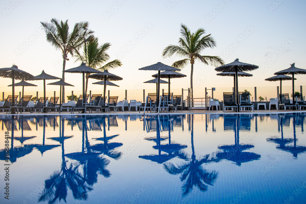 reflection of palm trees and umberllas in a swimming pool of empty lonely holiday resort vacated abandoned due to covid 19 