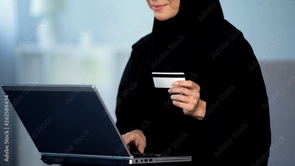 Pretty female in hijab entering credit card number on laptop, shopping online Pretty female in hijab entering credit card number on laptop, shopping online