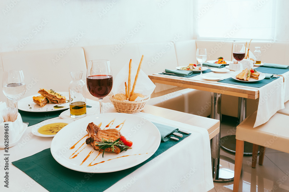Dining setup with wine and water glasses, cutlery in green napkins, food served on white plates, arranged by catering service in a modern light restaurant, cafe. Italian European cuisine