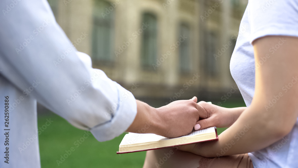 Couple holding hands, woman reading book, choice between study and relations Couple holding hands, woman reading book, choice between study and relations