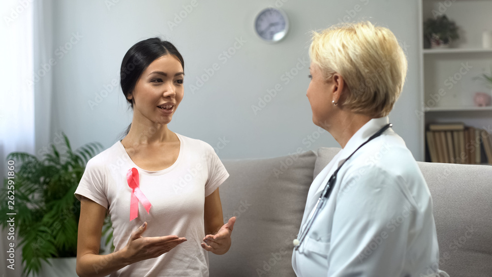 Female volunteer wearing pink ribbon talking to doctor, information in clinic Female volunteer wearing pink ribbon talking to doctor, information in clinic