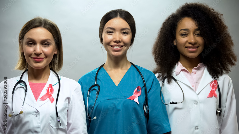 Group of smiling nurses with pink ribbons, breast cancer awareness, treatment Group of smiling nurses with pink ribbons, breast cancer awareness, treatment