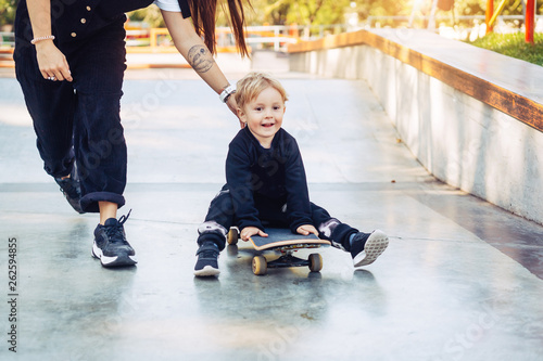 Young mother teaches her little boy to ride a skateboard