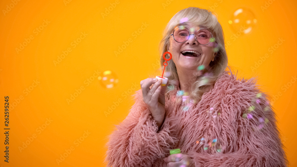 Funny stylish granny in pink coat and round sunglasses making soap bubbles, ad - obrazy, fototapety, plakaty 