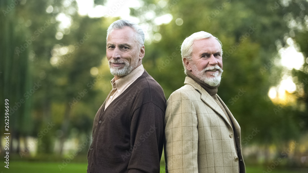 Confident pensioners standing back-to-back and smiling for camera, companions Confident pensioners standing back-to-back and smiling for camera, companions