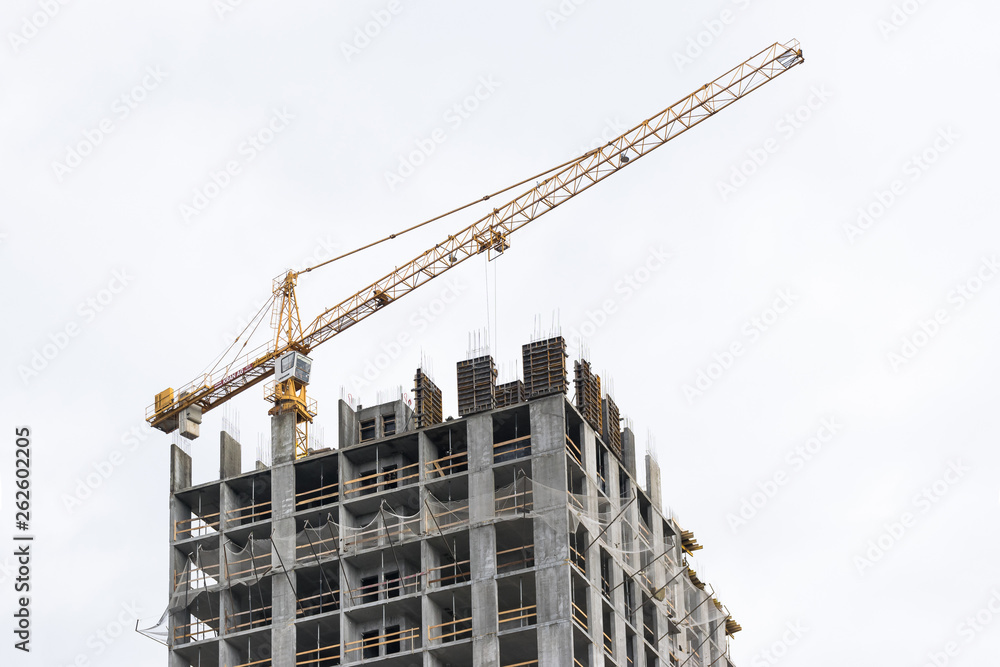High-rise building crane with a long arrow of yellow color against the sky above a concrete building under construction with brick walls