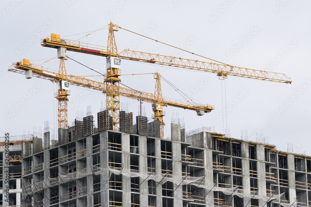 High-rise building crane with a long arrow of yellow color against the sky above a concrete building under construction with brick walls