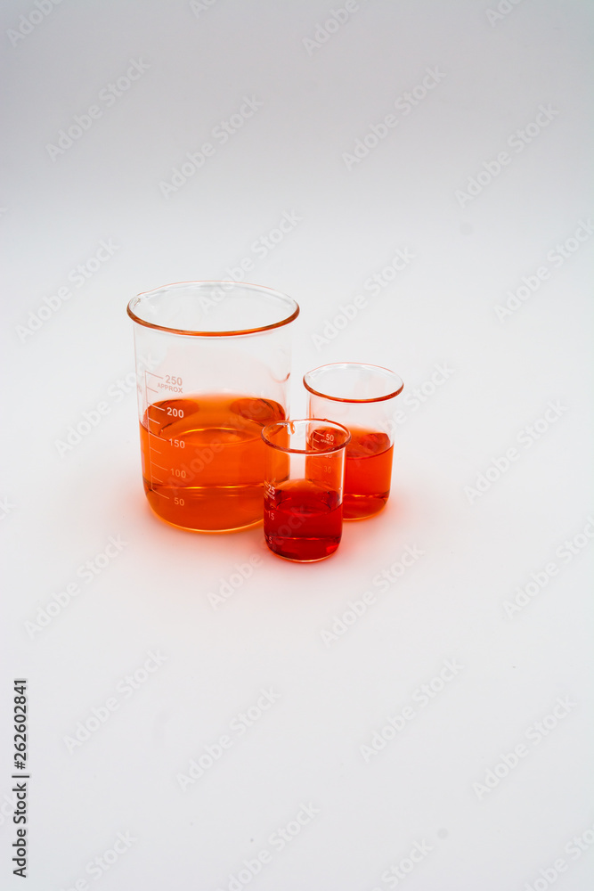 Vertical image of three science beakers filled with orange and red liquid set to the right side of the screen on a white background Vertical image of three science beakers filled with orange and red liquid set to the right side of the screen on a white background