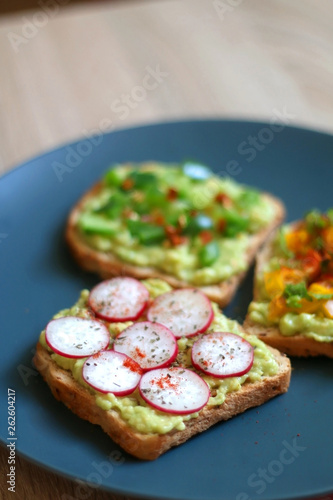 Three slices of toast with mashed avocado and various vegetable and herb toppings. Selective focus.