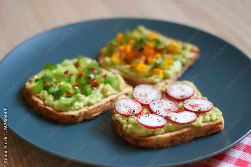 Three slices of toast with mashed avocado and various vegetable and herb toppings. Selective focus.