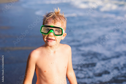 Child boy playing in the waves on the beach in summer sunset, kid watching sea waves and having fun © Lena May
