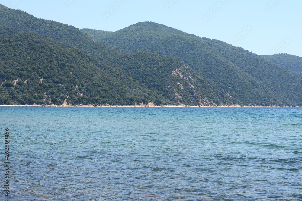 Beautiful minimalistic seascape of calm sea, sandy beach, blue sky, Greece. Horizontal.