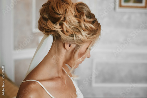 Beautiful blonde young woman with stylish wedding hairstyle in fashionable white lace lingerie posing at vintage interior
