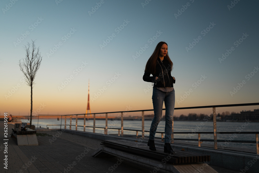 Fototapeta premium Young woman feeling confident during a lifestyle walk along the River Daugava at a sunset