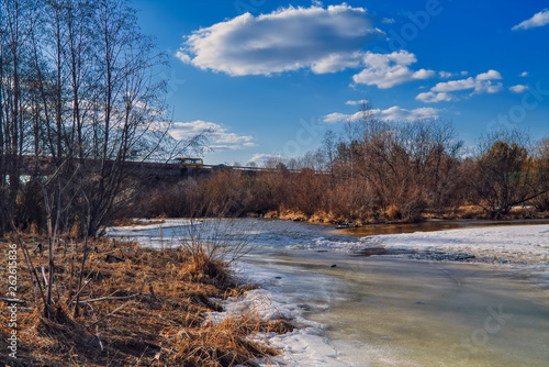 Fototapeta Naklejka Na Ścianę i Meble -  Early Spring landscape melts ice on a small river at the edge of the village.