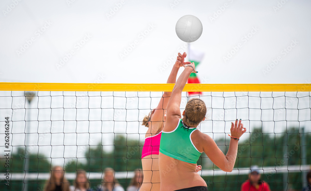 An athletic woman jumping to make wall block at beach volleyball net. Stretched arms and open hands to defend