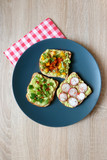 Three slices of toast with mashed avocado and various vegetable and herb toppings. Top view.