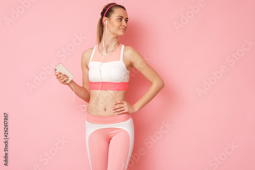 Beautiful woman is posing in sport clothes holding a phone in a hand.