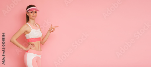 Lady in pink sport clothes isolated on pink background pointed by finger.