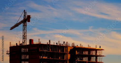 Fast motion timelapse of big crane silhouette and many workers building new construction under a beautiful colorful sunset sky