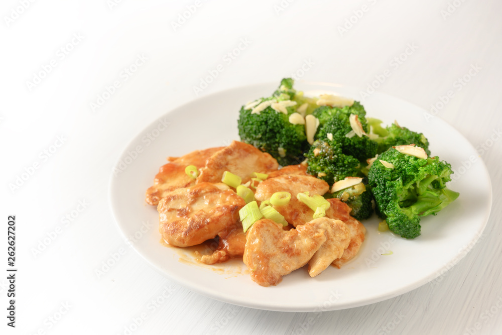 marinated chicken breast fillet with spring onions and broccoli with almond sticks as a healthy meal with little carbohydrates for slimming on a plate, background is blending to white, copy space marinated chicken breast fillet with spring onions and broccoli with almond sticks as a healthy meal with little carbohydrates for slimming on a plate, background is blending to white, copy space