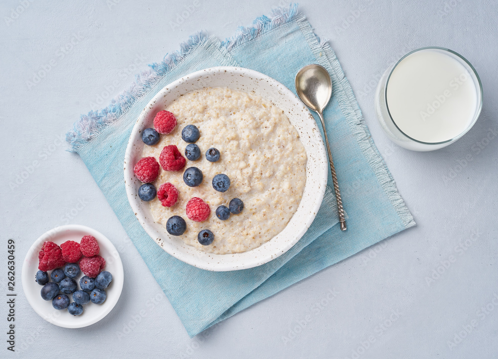 Oatmeal with blueberries, raspberries and cup of milk on blue light background. Top view. Healthy diet breakfast Oatmeal with blueberries, raspberries and cup of milk on blue light background. Top view. Healthy diet breakfast