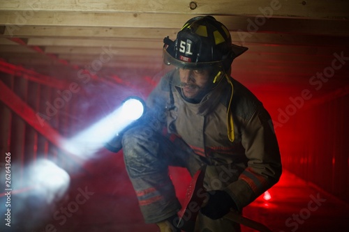 Firefighter in confined space with smoke searching for victims with large flashlight 