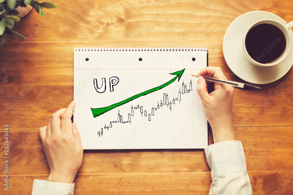 Market up trend chart with a person holding a pen on a wooden desk Market up trend chart with a person holding a pen on a wooden desk