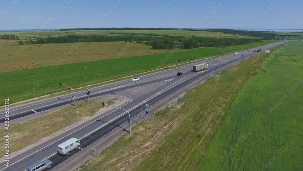 The intersection of highways. The movement of cars on the road. Top view of the intersection, cars, field and river. Summer video from the drone. Rural landscape. The intersection of highways. The movement of cars on the road. Top view of the intersection, cars, field and river. Summer video from the drone. Rural landscape.