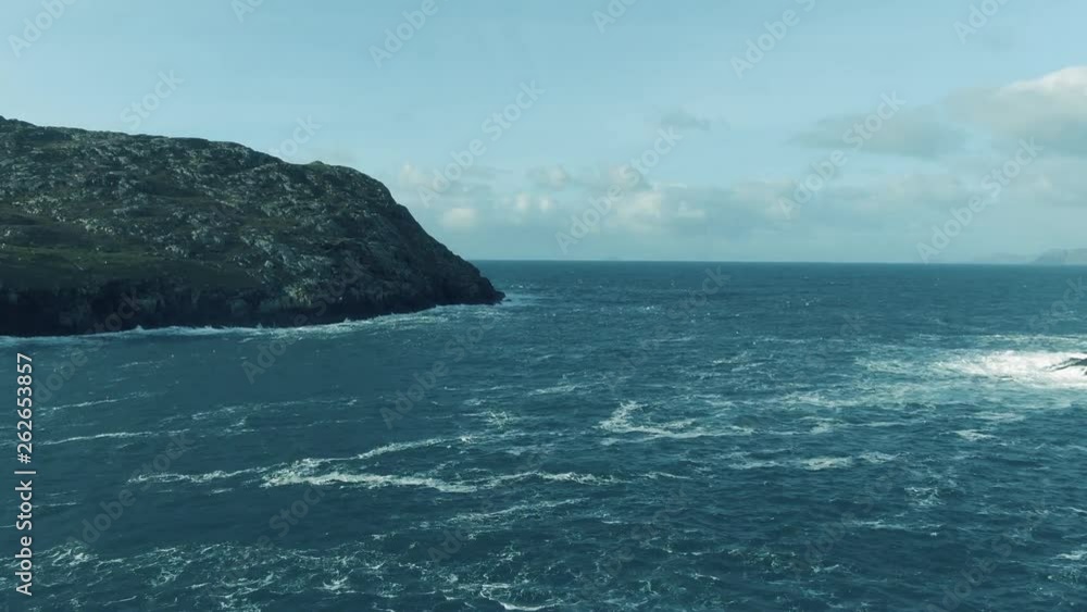 Aerial flight up away from the rocky irish shoreline with waves crashing upon the rocks towards Dursey Island in the distance with rough waters below Aerial flight up away from the rocky irish shoreline with waves crashing upon the rocks towards Dursey Island in the distance with rough waters below