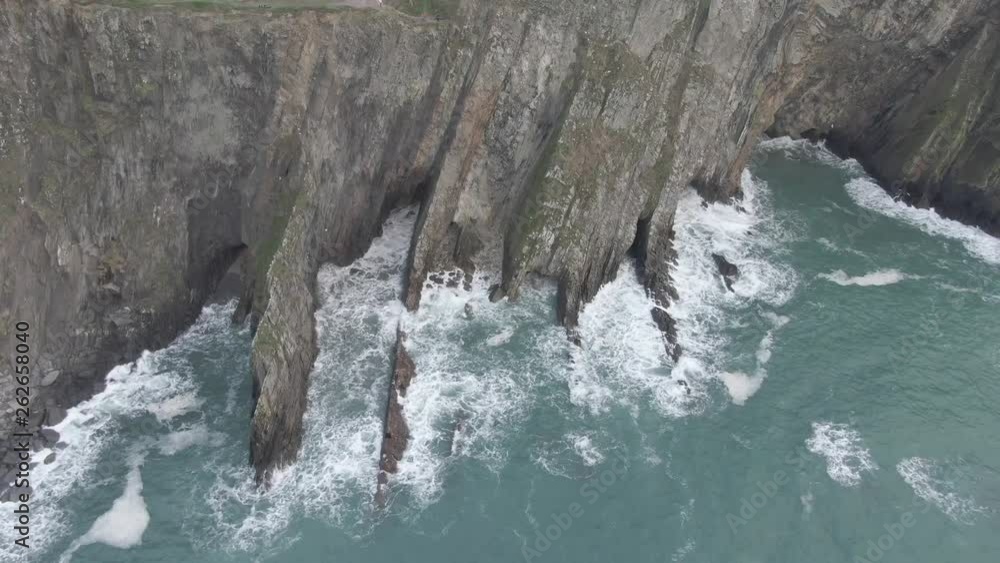 Slow aerial slide of irish sea side cliffs with rough seas and waves hitting the cliffs Slow aerial slide of irish sea side cliffs with rough seas and waves hitting the cliffs