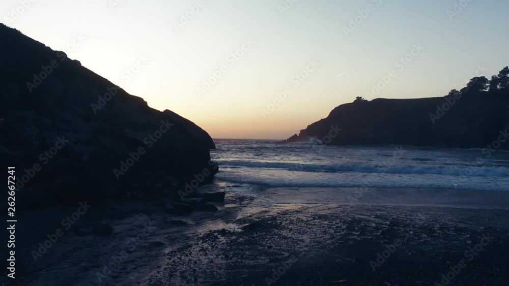 Drone captures a setting sun at golden hour over a lonely cove. Haze and setting sun create a dreamy and surreal vibe.