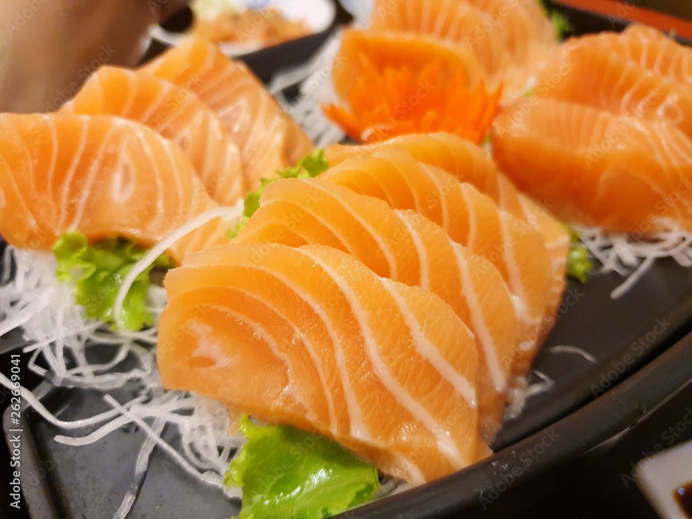 Japanese food style, Top view of salmon slice on radish and lettuce on black plate, Salmon sashimi is Japanese traditional, Selective focus