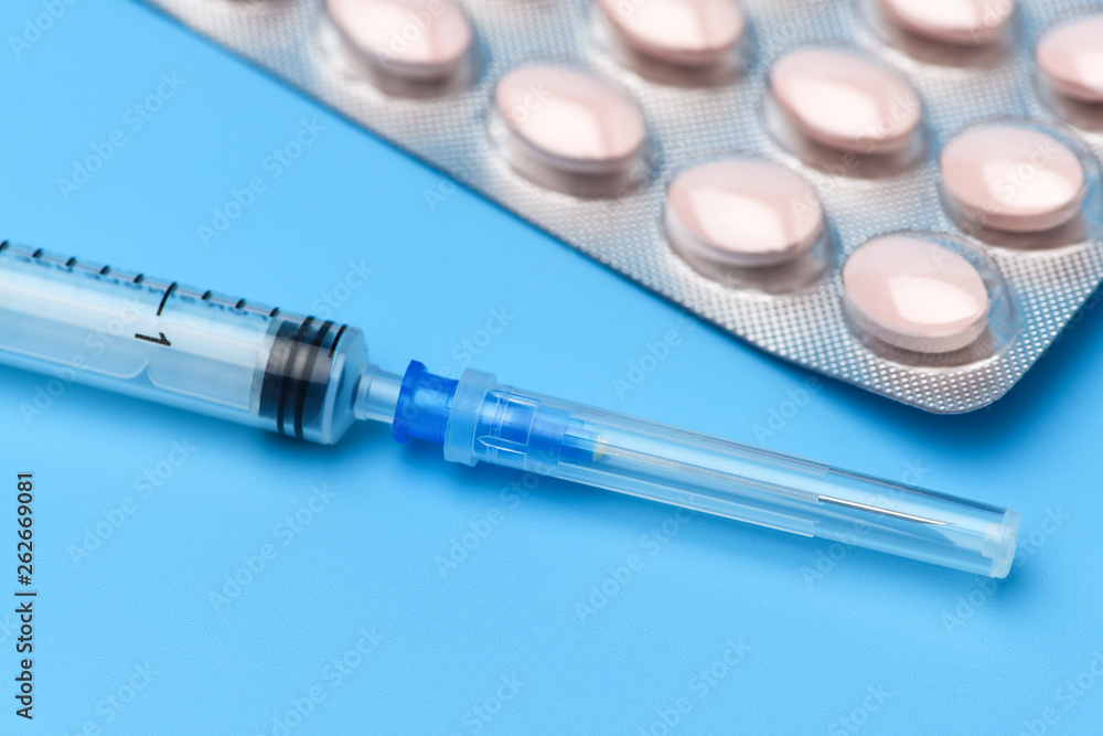 Many tablets are on a blue background, at the bottom is a syringe with an injection. Drugs and pills prescription background. Pharmaceutical preparation. Many tablets are on a blue background, at the bottom is a syringe with an injection. Drugs and pills prescription background. Pharmaceutical preparation.