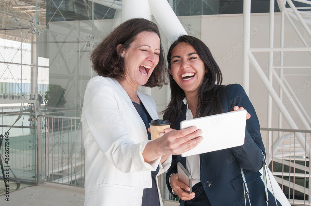 Two business women using tablet and laughing in office hall