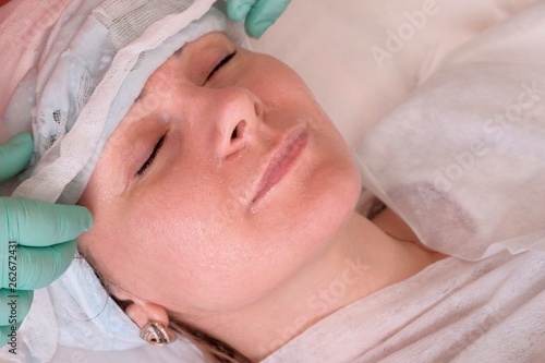 The beautician removes the gauze alginate mask from the face of the girl-client. Cosmetic procedures for face care. Moisturizing and nourishing the skin.