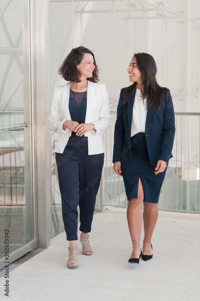 Fototapeta premium Two smiling female coworkers walking in office hall